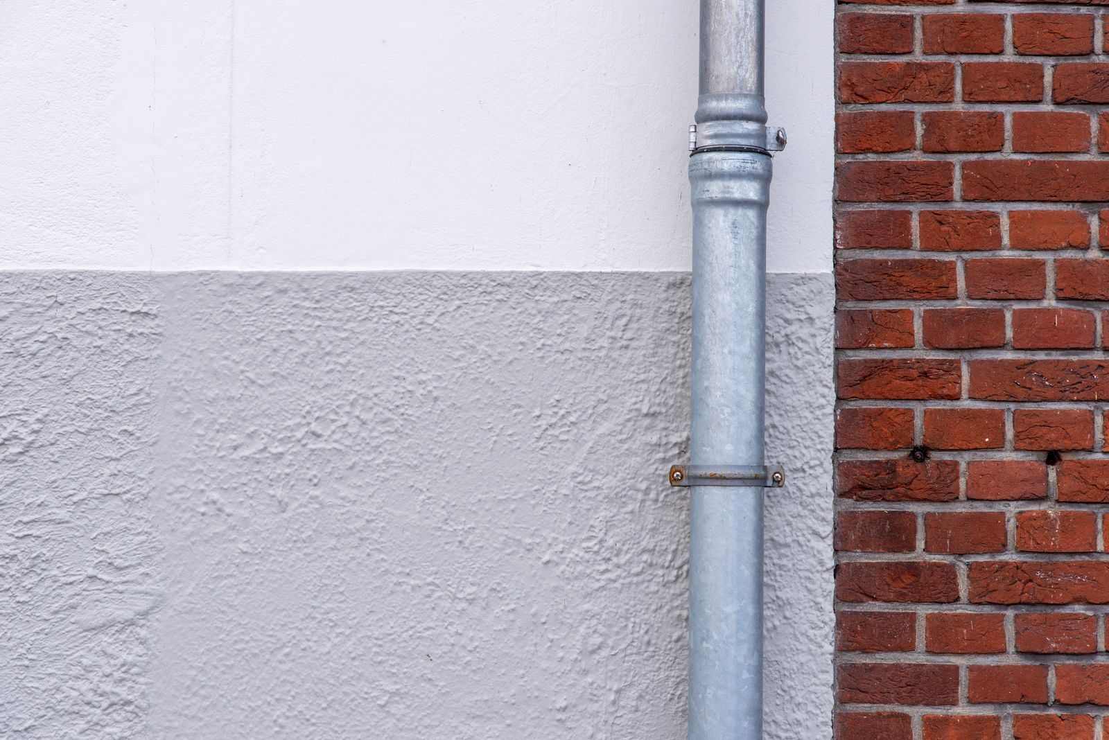 A downpipe running down a white and brick house wall